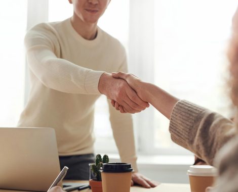 Two people shaking hands in an office setting, symbolizing agreement, partnership, and collaboration.